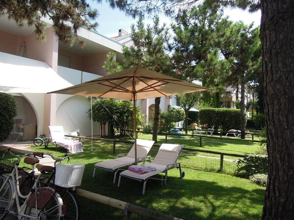 A courtyard with two lounge chairs, a bicycle, and a covered seating area. - Relaxing Apartment With Garden and Pool (San Michele al Tagliamento)