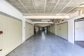 A long, empty corridor with closed doors on both sides, a concrete ceiling with visible pipes, and a smooth floor.