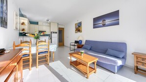 A living room with a sofa, wooden coffee table, and a dining area with chairs and a table. - RESIDENCIAL ALMADRAVA 2 Roses (Rosas / Roses)