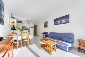 A compact living space with a dining area, a sofa, a coffee table, and a kitchen in the background.