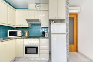 A compact kitchen with a microwave, toaster, and oven. There is a clock on the wall and an air conditioner above the door.