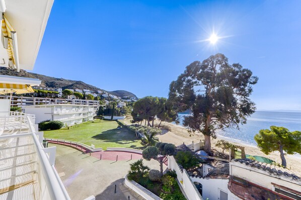 A coastal hotel with a view of the sea, a large tree, and a well-maintained garden.