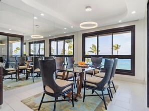 A modern dining area with a glass table, wicker chairs, and a view of the ocean.