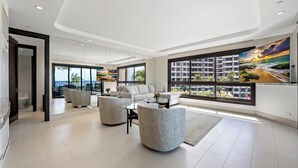 Un vaste espace de vie doté d’une grande fenêtre offrant une vue sur la mer et les bâtiments, d’un canapé moderne et d’une table à manger.