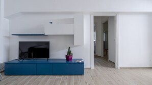 A modern living room with a flat-screen TV, a blue entertainment unit, and a potted cactus. - Appartamento Ecate (Ragusa)
