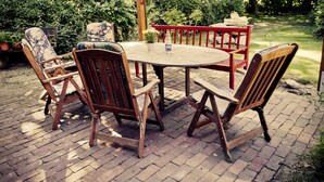 Een houten terras buiten met een ronde tafel en zes stoelen.