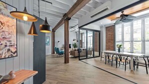 Un bureau à aire ouverte avec des poutres en bois apparentes, une longue table entourée de chaises et des luminaires suspendus.