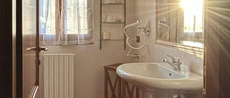 A bathroom with a radiator, a sink, a mirror, and a window with curtains.