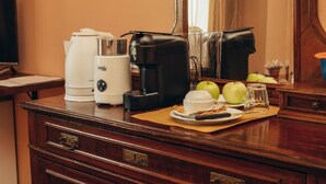 A hotel room with a wooden desk, a coffee maker, a tea maker, and a fruit bowl with apples and a glass.