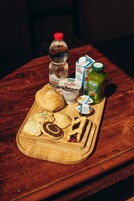 Uma mesa de madeira com uma bandeja contendo uma garrafa de água, um pacote de leite, uma garrafa de suco, um pote de iogurte, um muffin, um biscoito e um pastel.