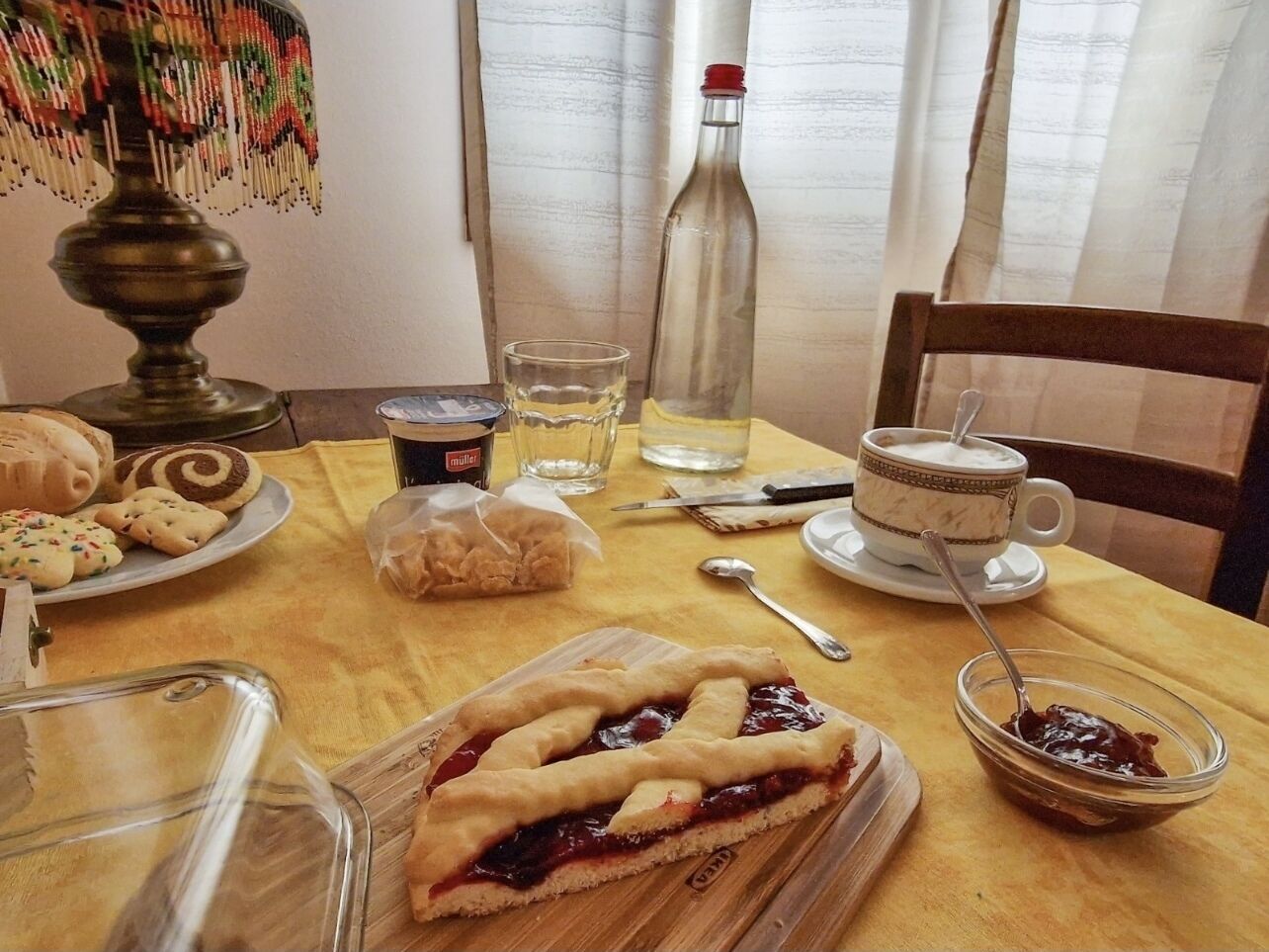 A dining table with a variety of food items, including a pie, cookies, and a bottle of water.