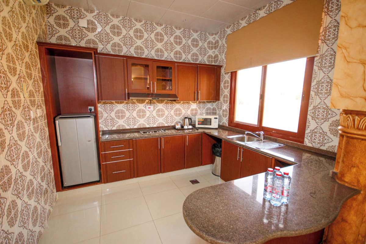 A kitchen with patterned wallpaper, wooden cabinets, a refrigerator, a microwave, and a sink.