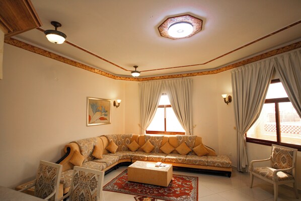 Una sala de estar con un amplio sofá en forma de L, una mesa de centro, sillas con estampado y un candelabro en el techo.