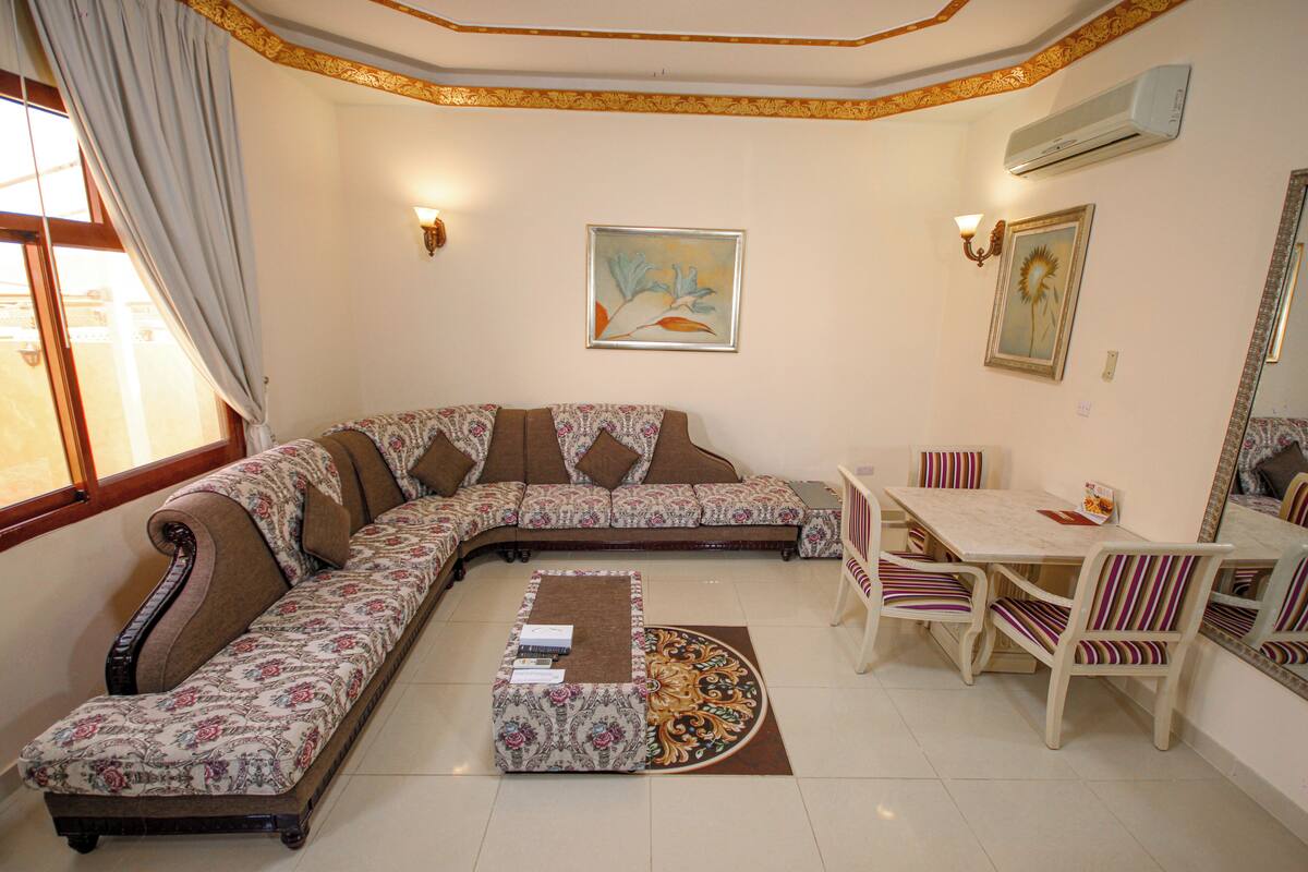 A living room with a sofa, a dining table with chairs, a patterned rug, and artwork on the walls.