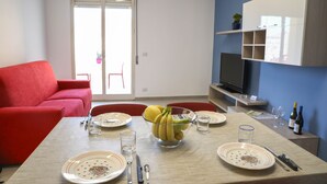 A dining area with a table set for four, a red sofa, a TV, and a blue wall. - Appartamento Orfeo (Ragusa)