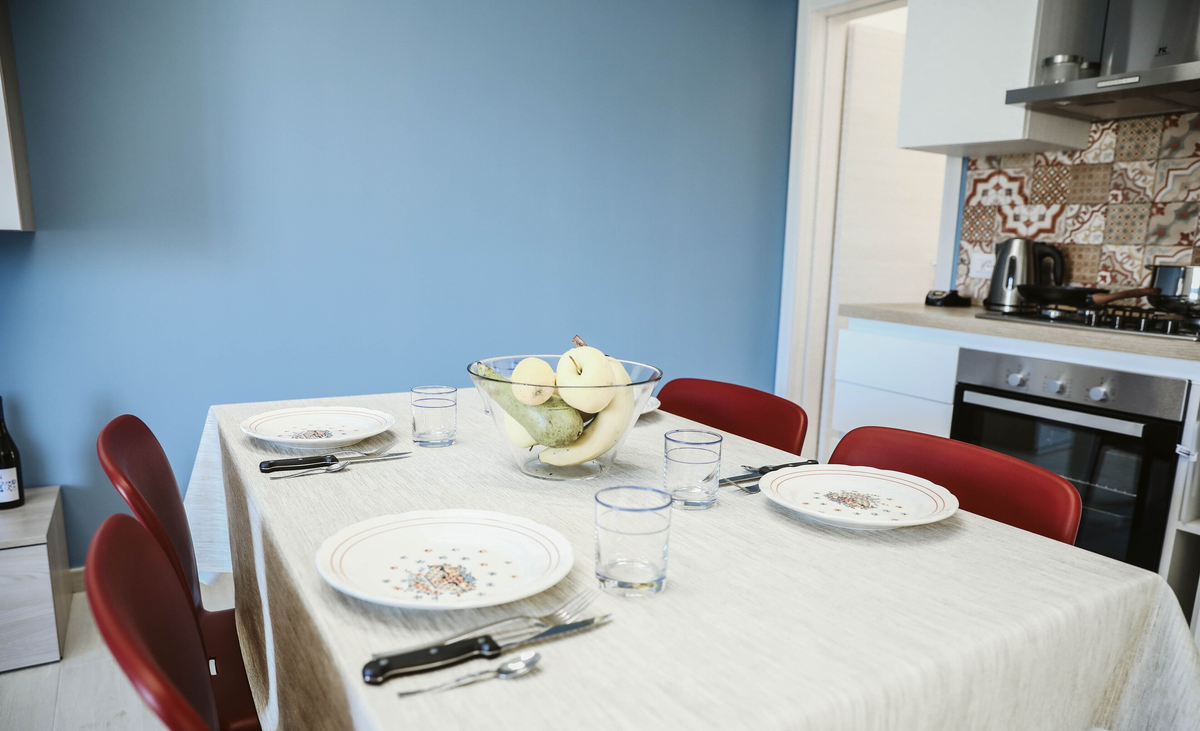 Een eettafel gedekt met borden, bestek en een schaal fruit.