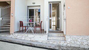 A building entrance with a stone staircase leading up to a door, a metal gate, and a small table with chairs outside. - Appartamento Orfeo (Ragusa)