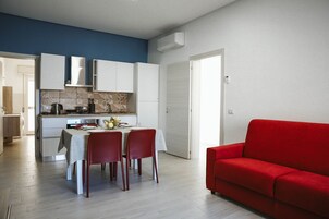 Una cocina moderna con armarios blancos, una mesa de comedor con cuatro sillas y un sofá rojo en la sala.