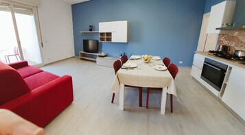 Una sala de estar moderna con un sofá rojo, una mesa de comedor para cuatro personas y una cocina con estufa y horno.