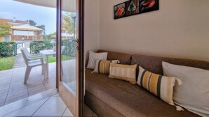 Una sala de estar con un sofá, un ventanal de vidrio que da a un patio y un cuadro en la pared.
