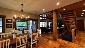 A spacious dining area with wooden furniture and a chandelier, a cozy living room with a fireplace, and a wooden staircase. - The Lake House on Otisco Lake, stunning family getaway (Marietta)