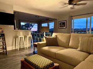 A living room with a sofa, a coffee table, a lamp, and a view through large windows.