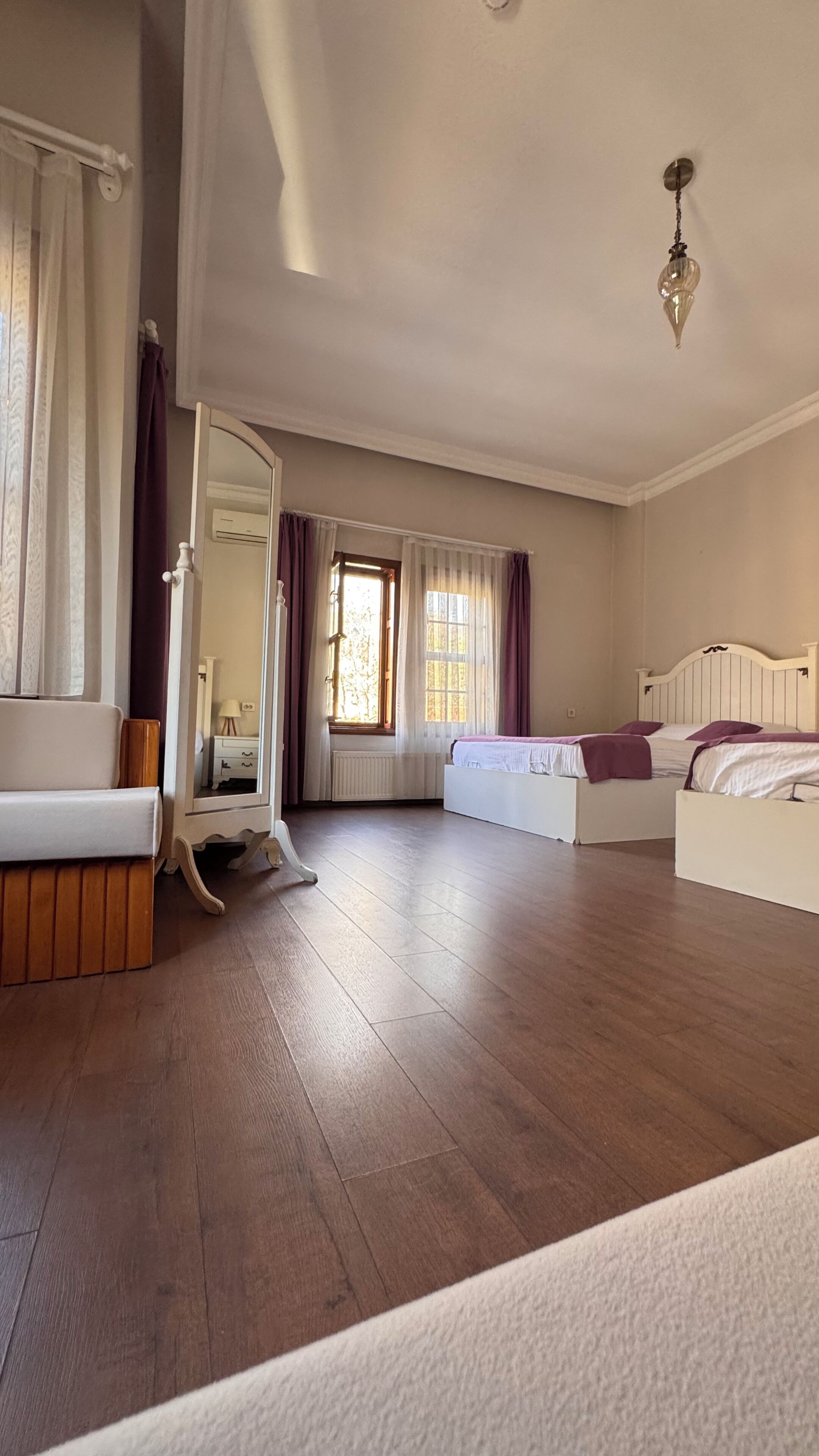 A spacious room with a large bed, a smaller bed, a vanity with a mirror, and a window with curtains.