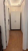Un pasillo con una puerta doble blanca, piso de madera y techo con iluminación empotrada.