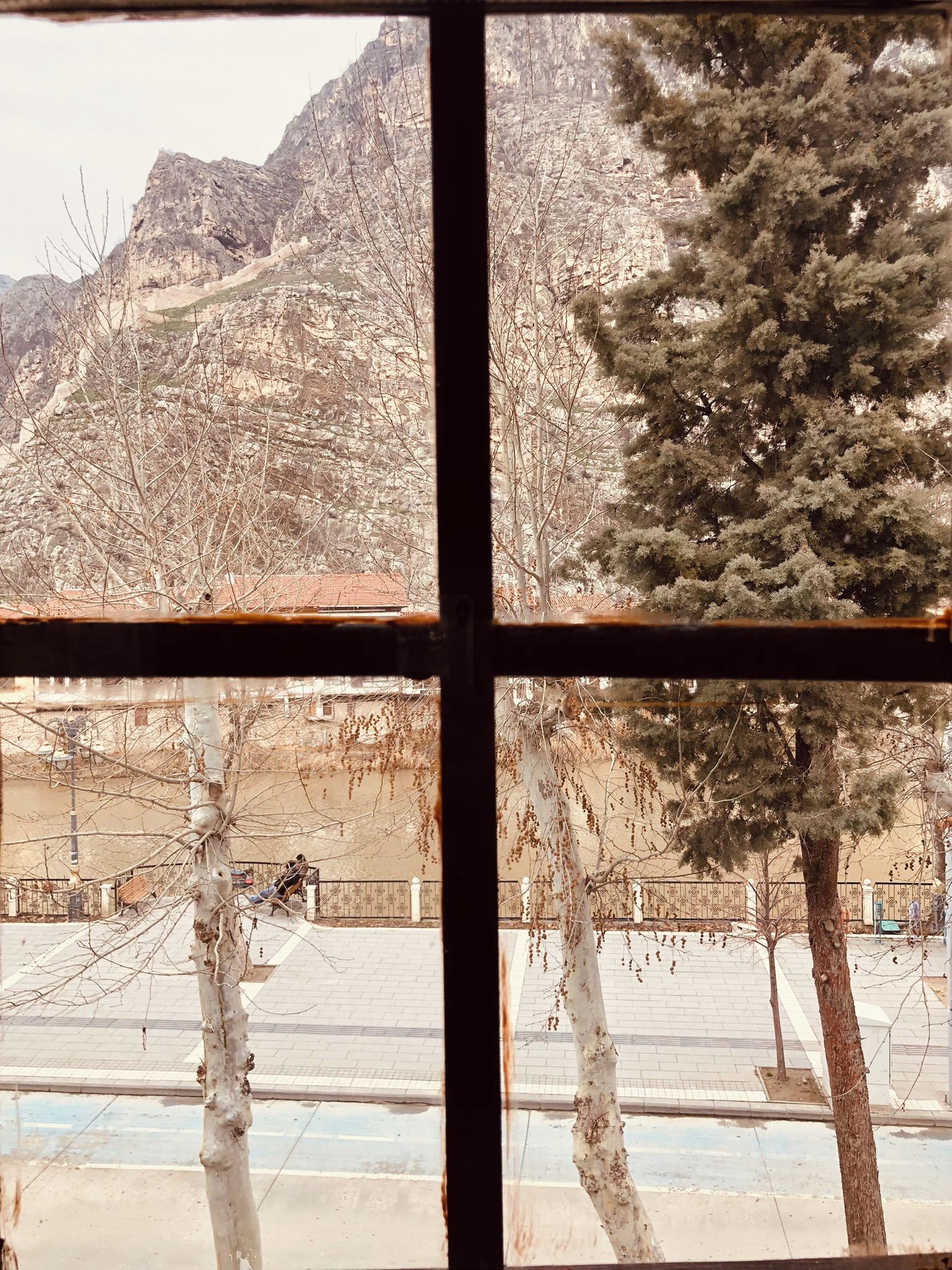 Vista da janela mostrando uma paisagem montanhosa com árvores e um edifício ao longe.