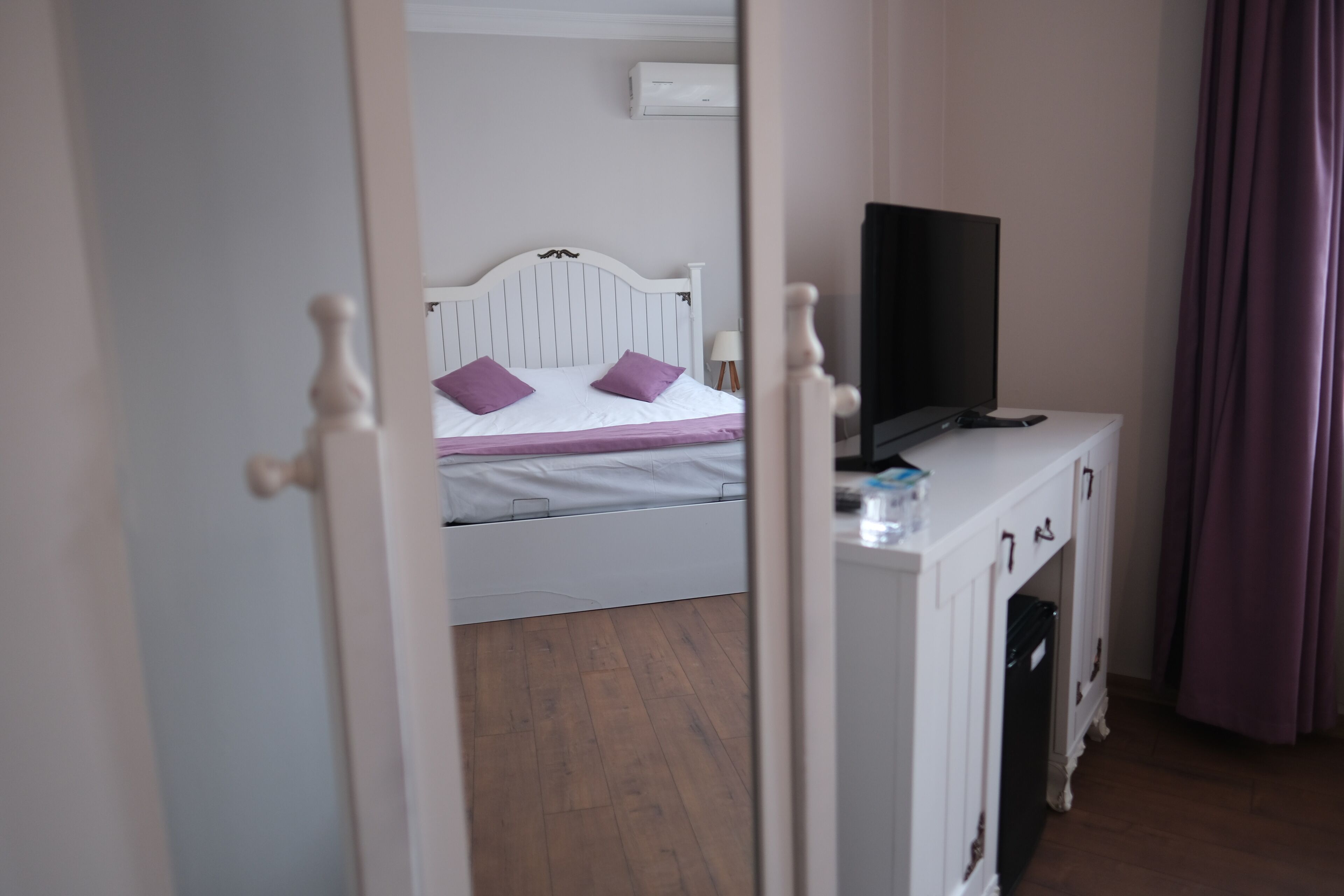 Um quarto com cama, televisão sobre um móvel e porta que dá para outro espaço.