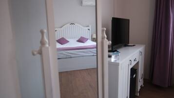 Um quarto com cama, televisão sobre um móvel e porta que dá para outro espaço.