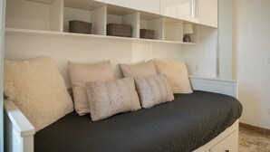 Un lit avec une couette sombre, quatre oreillers et une tête de lit blanche. Il y a des étagères de rangement au-dessus du lit.
