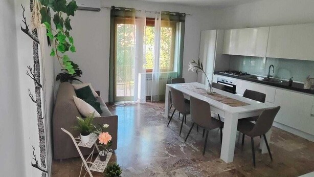Une cuisine moderne avec des meubles blancs, un coin repas comprenant une table et des chaises blanches, et un canapé avec une table d’appoint.