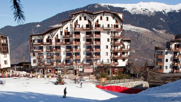 A multi-story hotel with balconies, ski slopes, and snow-covered mountains in the background. - Renovated apartment in La Tania center with parking (Courchevel)