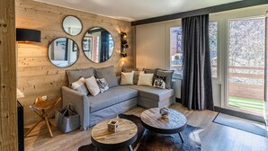 A modern living room with a grey sectional sofa, two round coffee tables, and a wooden wall with three mirrors. - Renovated apartment in La Tania center with parking (Courchevel)