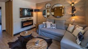 A modern living room with a grey sofa, a fireplace, and a TV mounted on the wall. - Renovated apartment in La Tania center with parking (Courchevel)