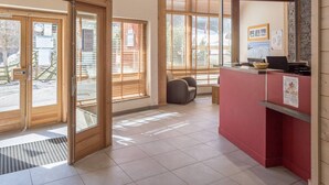 A hotel lobby with a reception desk, a seating area, and large windows with blinds. - Renovated apartment in La Tania center with parking (Courchevel)