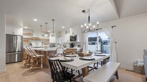 Une cuisine moderne avec des meubles blancs, des appareils en acier inoxydable et un îlot central. On y trouve également un coin repas avec une table et des chaises blanches.