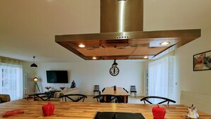 Una cocina moderna con una placa de inducción Bosch, una campana extractora de acero inoxidable y un comedor con una mesa y sillas de madera.