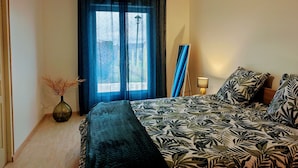 Un dormitorio con cama, ventana con cortinas, un jarrón con plantas secas y una lámpara.