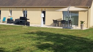 Un edificio con techo de tejas, un patio con mobiliario exterior y una entrada con puerta de vidrio.