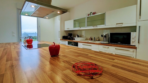Una cocina moderna con piso de madera, extractor de acero inoxidable, armarios blancos y vista al exterior.