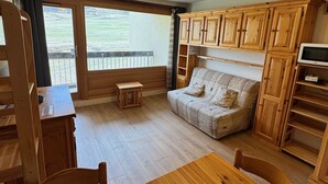 Una habitación acogedora con un sofá de madera, una mesita pequeña y un televisor sobre un mueble de madera.