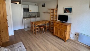 Cocina compacta con microondas, pileta y lavavajillas. Hay una mesa de comedor de madera con sillas y un televisor sobre un mueble de madera.