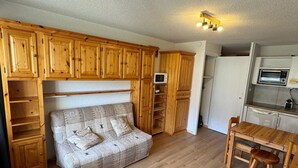Un espacio habitable compacto con sofá, armarios de madera, kitchenette y una mesa de comedor.