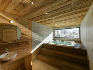 Un interior de madera con un ventanal grande, una bañera y un espejo redondo.