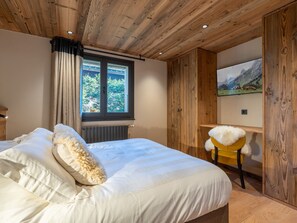 A bedroom with a wooden ceiling, a bed with white bedding, a window with curtains, a radiator, a wooden wardrobe, and a television on the wall. - 4★ Duplex in La Clusaz, 9 pers, private spa, 210 m to slopes, 4 bedrooms (La Clusaz)