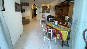 Ein kompakter Wohnbereich mit Essbereich, der einen Tisch mit Tassen und Teekanne, eine Couch und eine Küchenzeile mit Holzsärchen und einer Uhr zeigt.