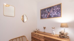 Une pièce comprenant une commode en bois, une chaise en osier, un miroir et un tableau encadré représentant un cerf.