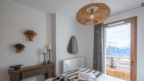 Une chambre à coucher avec un lit, une commode, un miroir et une vue sur les montagnes, visible à travers une porte.